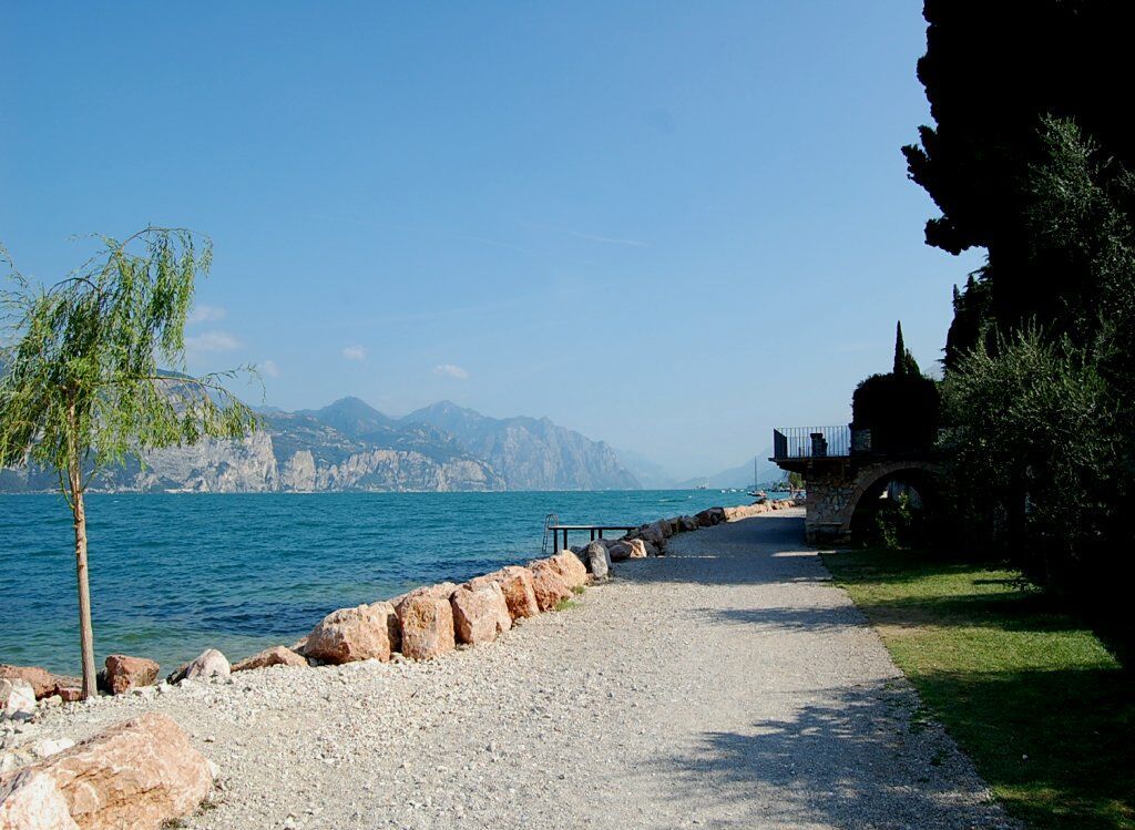 A gravel path leading to a body of water with a rocky shoreline and a small structure on the right.