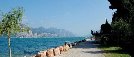 A gravel path leading to a body of water with a rocky shoreline and a small structure on the right.