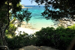A coastal landscape with clear turquoise waters, rocky beach, and dense greenery.