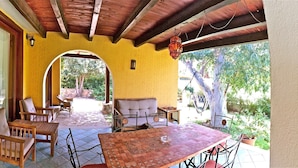 Un patio couvert, aménagé avec des meubles en bois, un sol carrelé et un mur jaune.