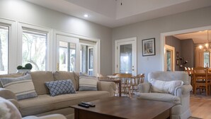 A spacious living room with a beige sofa, a wooden coffee table, and a dining area with a wooden table and chairs.