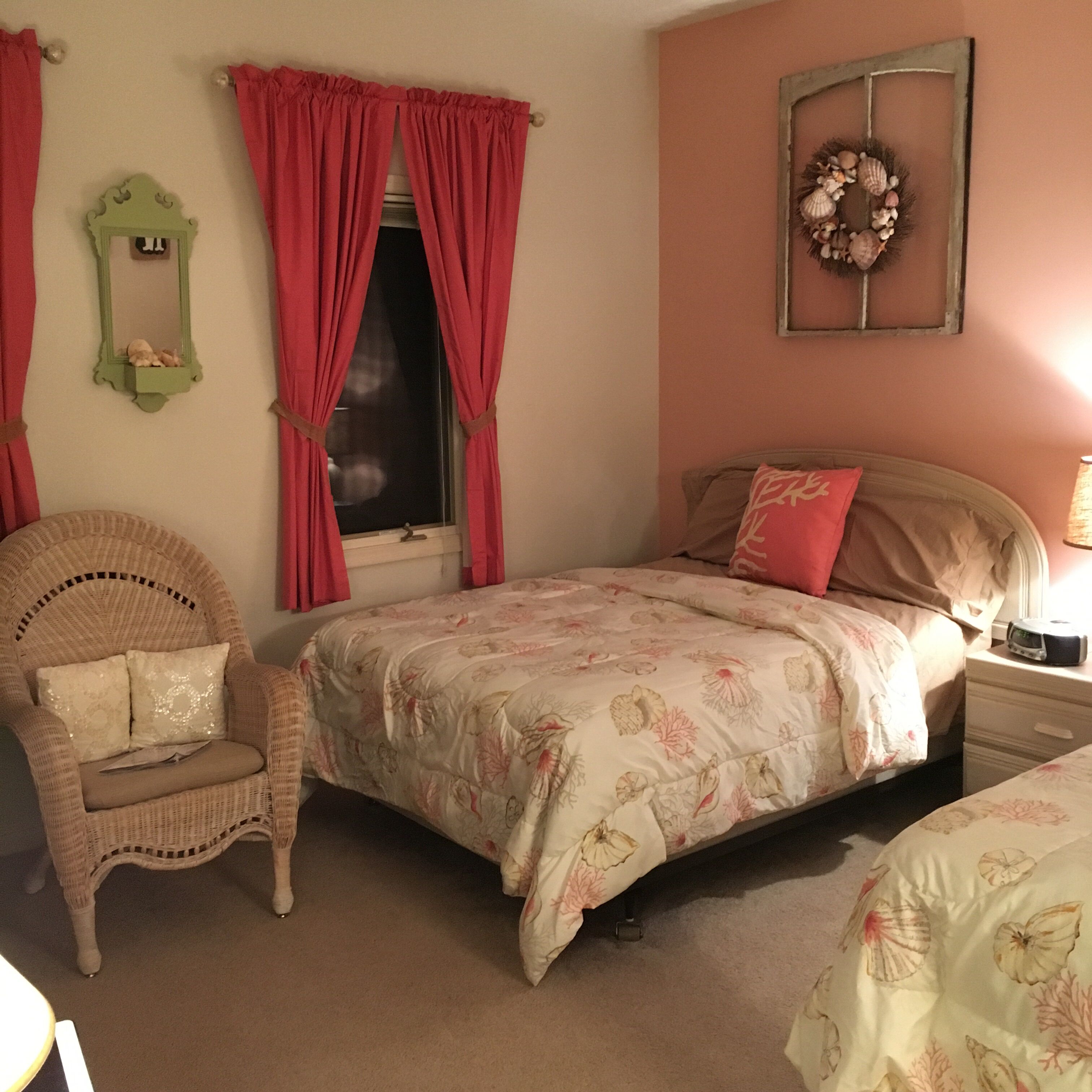 Une chambre à coucher comprenant un lit, une chaise, une table de chevet, un miroir mural et une fenêtre avec des rideaux.