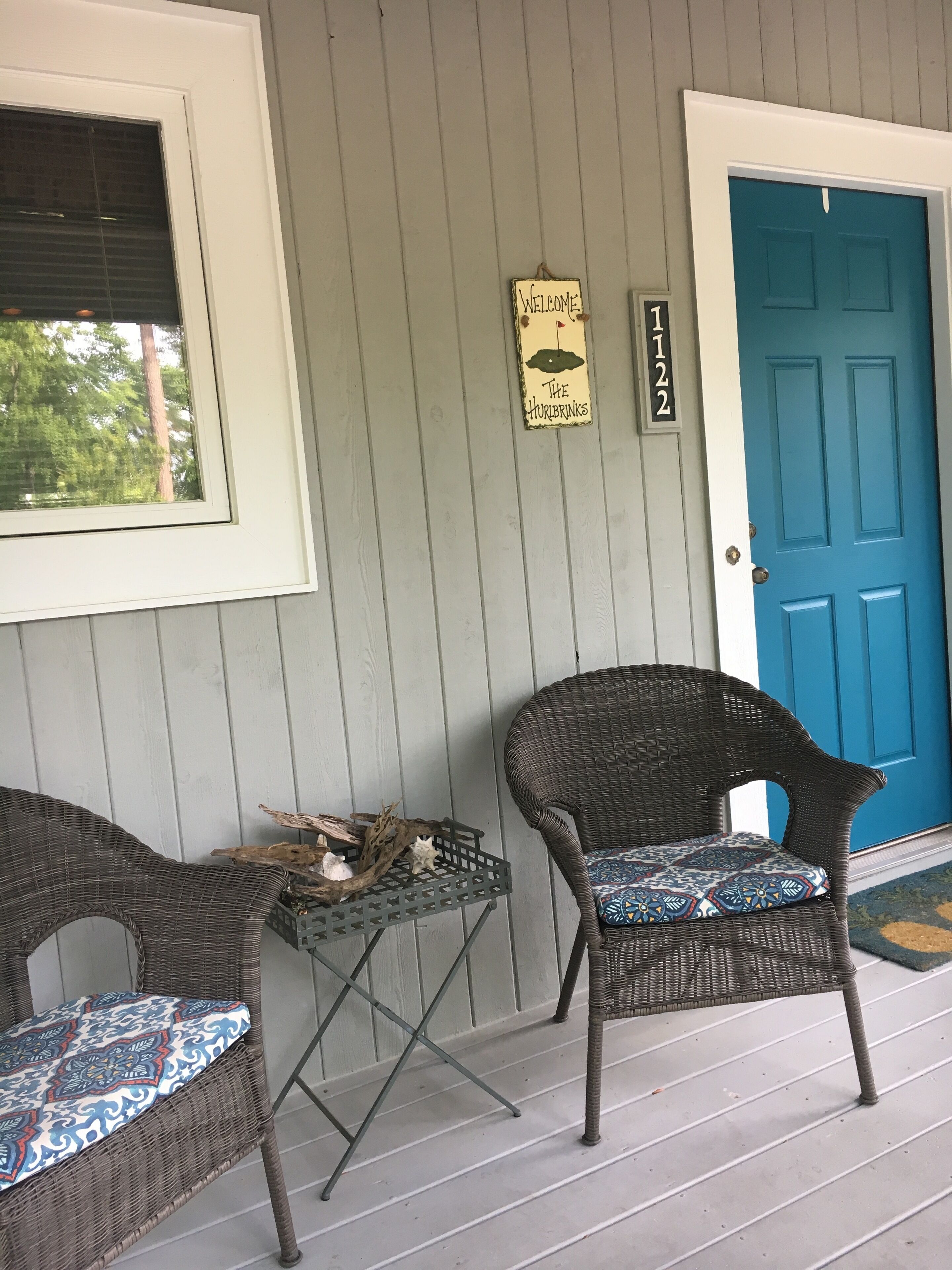 A porch with wicker furniture, a blue door, and a welcome sign.