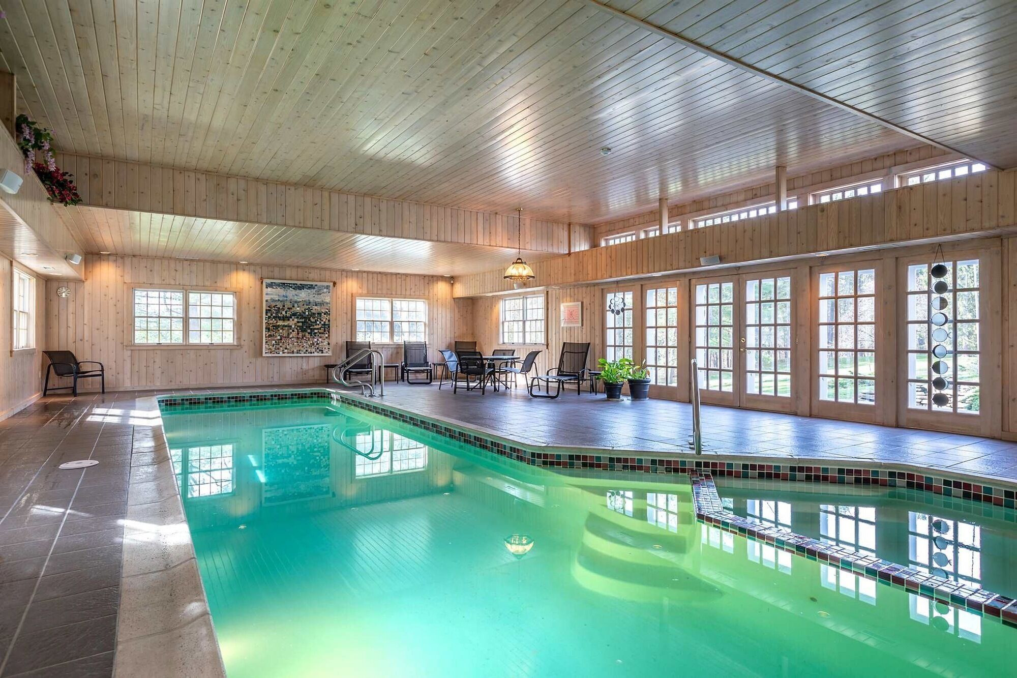 A large indoor swimming pool with a wooden interior, multiple windows, and seating areas.
