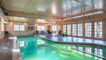 A large indoor swimming pool with a wooden interior, multiple windows, and seating areas.