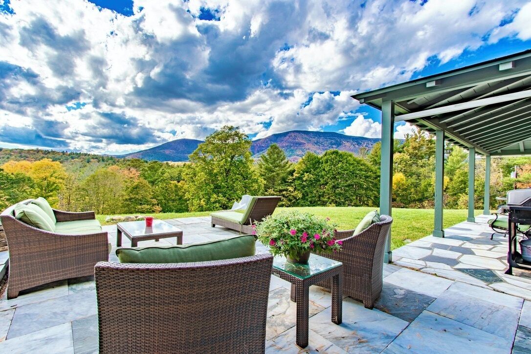 An outdoor patio with wicker furniture, a glass table, and a grill area.