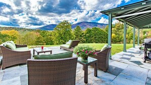 An outdoor patio with wicker furniture, a glass table, and a grill area. - The Privacy of a home & Perks of a Resort! Pool, Tennis, Views, Dogs, 6 baths! (Manchester)