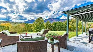 An outdoor patio with wicker furniture, a glass table, and a grill area.