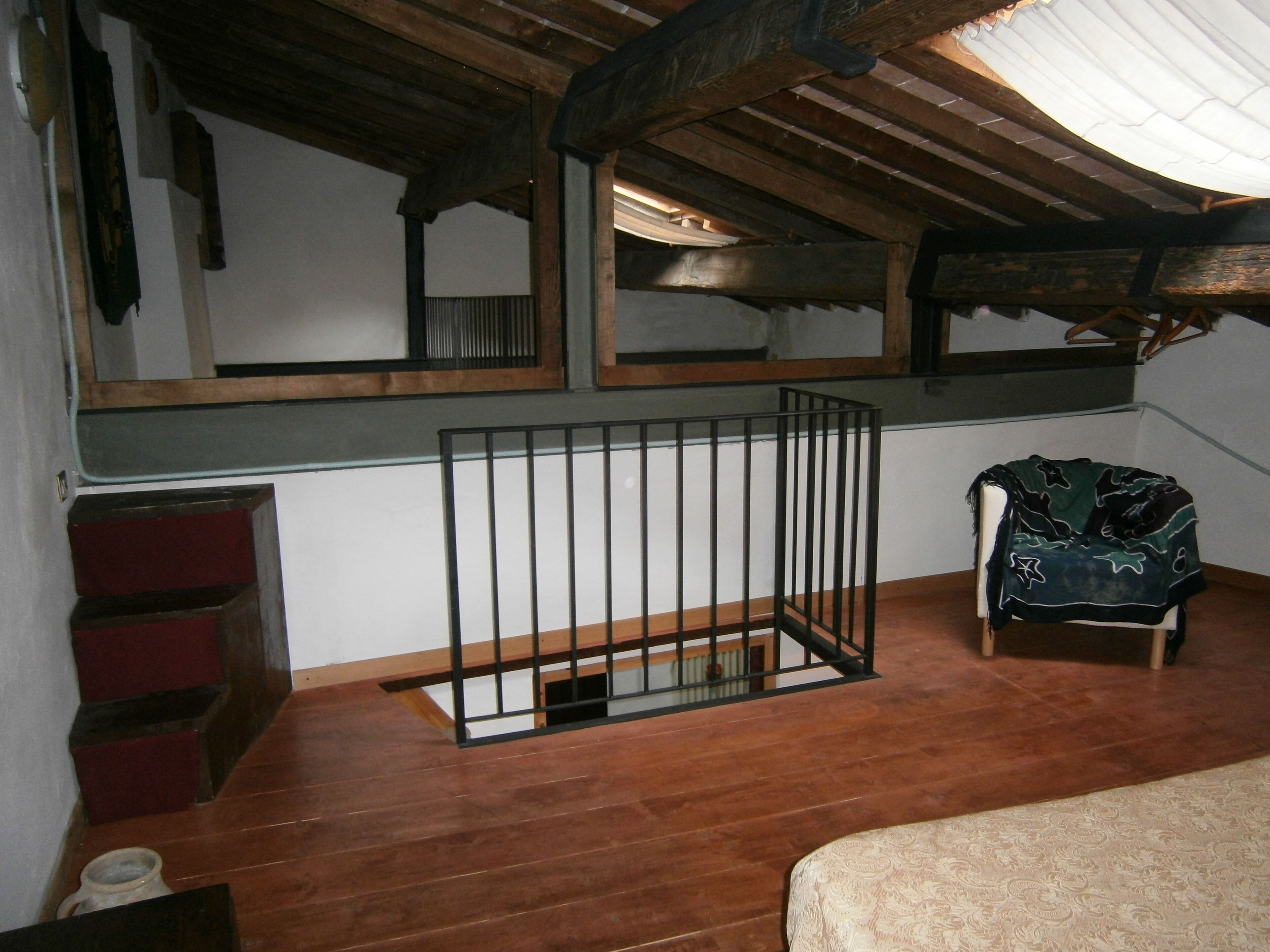 Une pièce avec un plancher en bois, un berceau en métal, une chaise recouverte d’une couverture et un lit avec une couvre-lit à motifs.