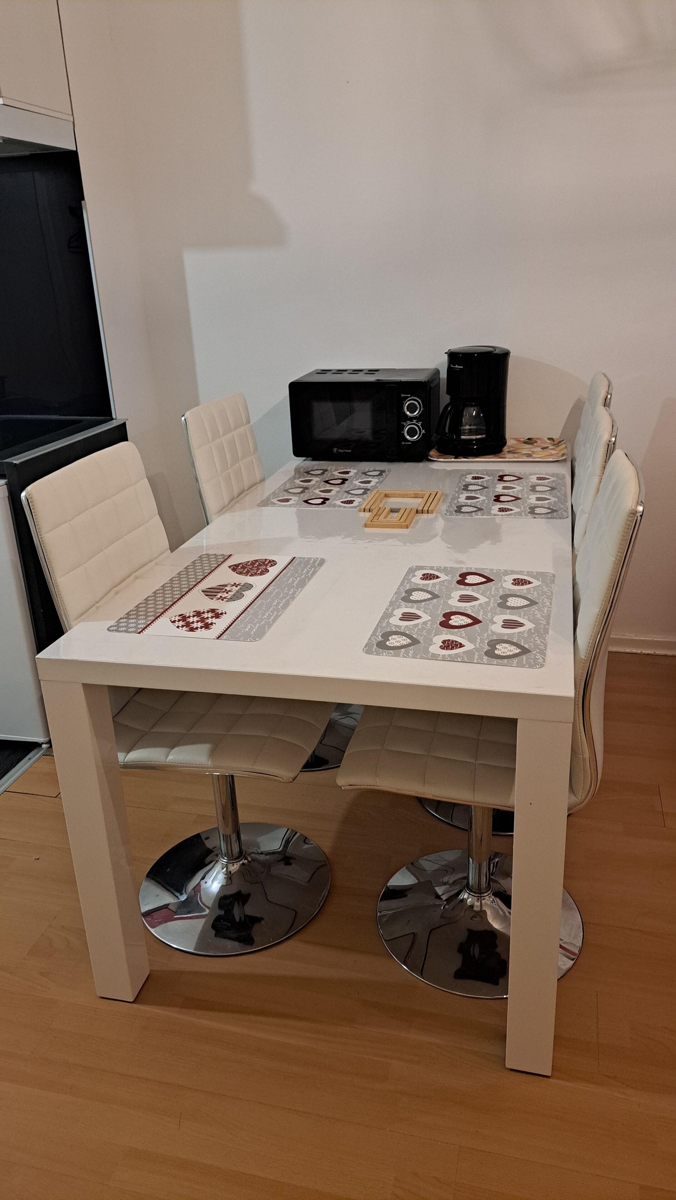 A dining table with a white tablecloth, two chairs, a coffee maker, and a microwave.