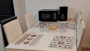 A dining table with a white tablecloth, two chairs, a coffee maker, and a microwave.