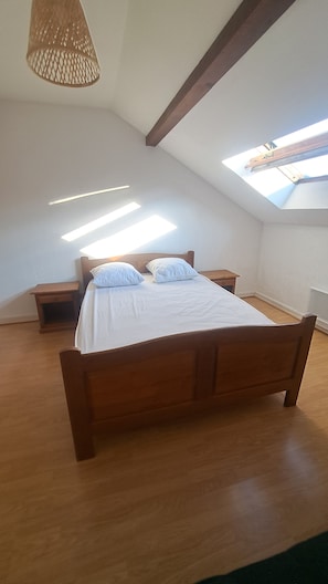 Quarto com teto inclinado, claraboia, cama de madeira e mesas de cabeceira.
