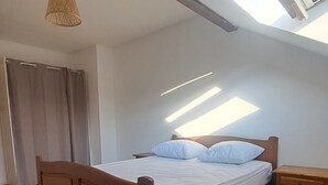 A bedroom with a wooden bed, a bedside table, a hanging light fixture, and skylights.