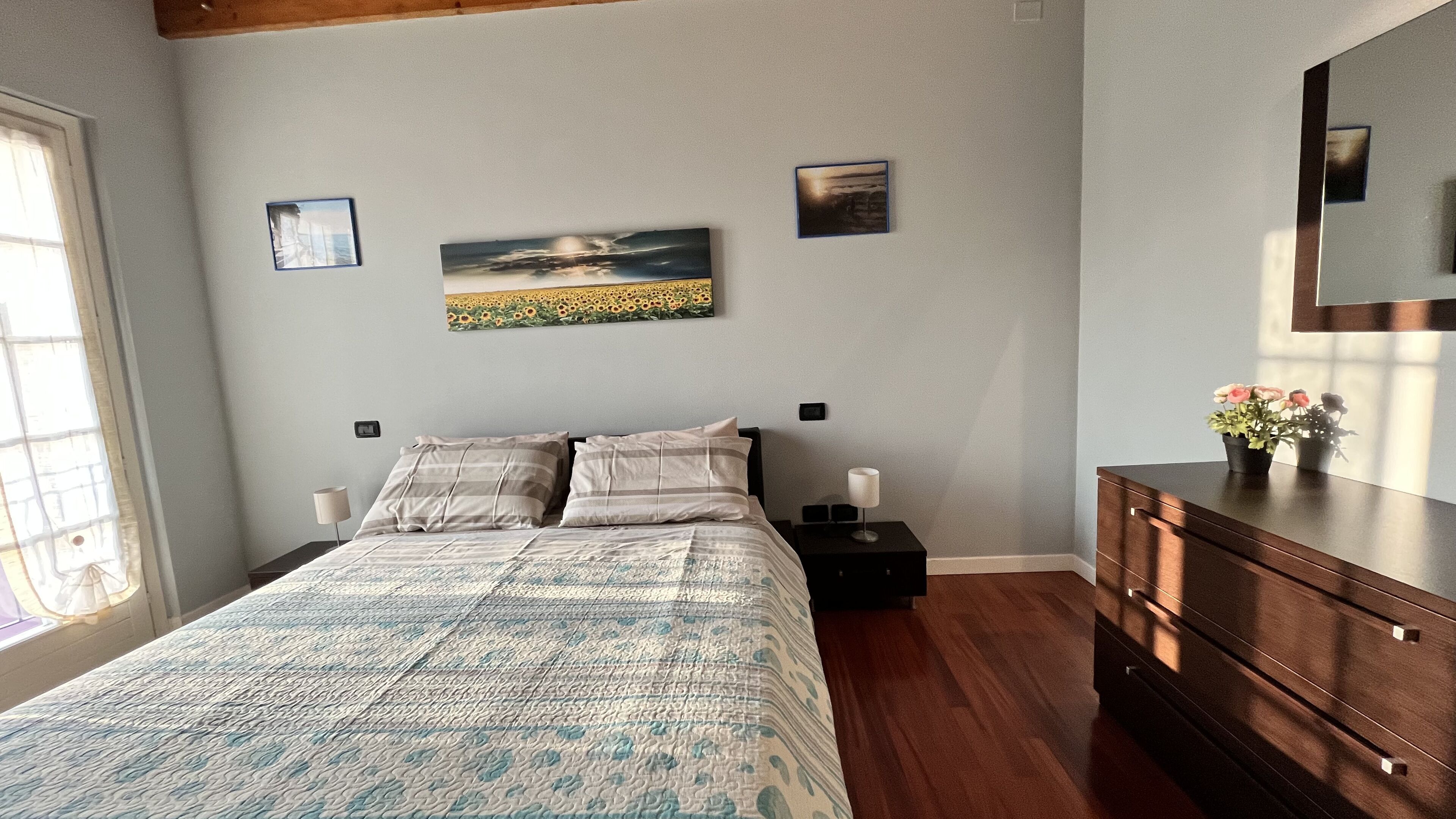 A bedroom with a bed, bedside tables, a dresser, and wall art.
