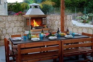 An outdoor dining area with a stone wall, a brick oven, and a table set for two with plates, glasses, and a bottle. - Georgios Rafaela Villa - Large Secluded Single Storey Stone Built Villa with 5 Bedrooms near Polis (Polis)