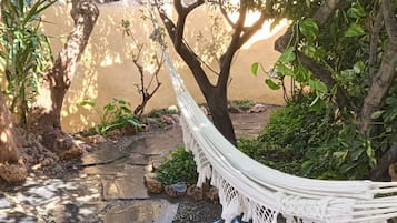Un hamac tendu entre deux arbres dans un jardin, avec un chemin pavé de pierres.