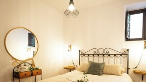 A neatly made bed with a headboard, a bedside table with a mirror, and a hanging light fixture. - Houses Amaro.   Spacious, comfortable, cozy and wonderful views  (0rgiva)