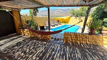 Une terrasse avec un hamac, une piscine et du mobilier d’extérieur.