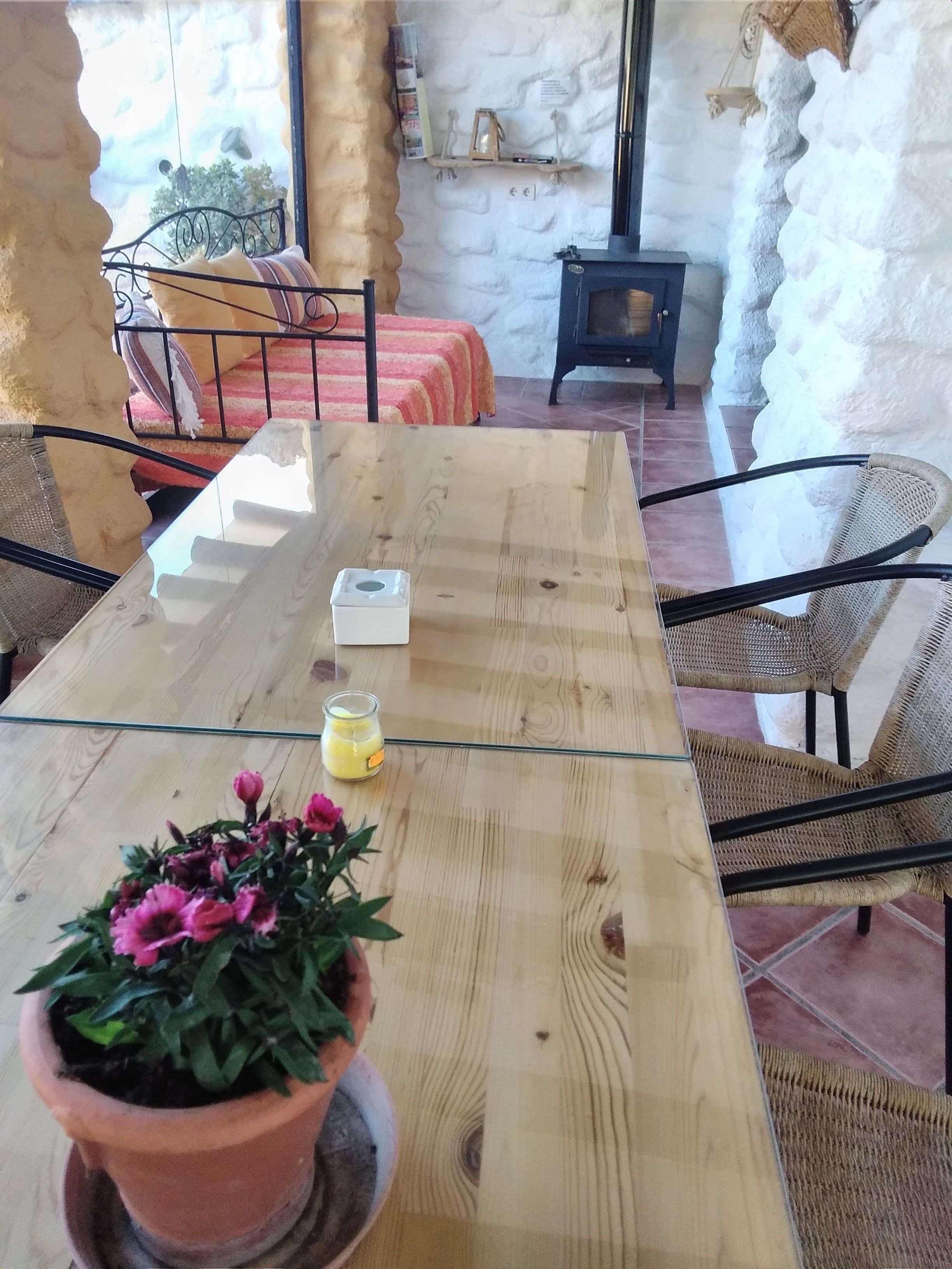 Een houten eettafel met een glazen blad, omringd door rieten stoelen, in een ruimte met stenen muren en een open haard.