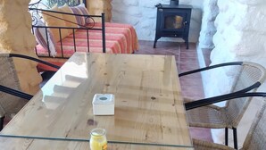 A wooden dining table with a glass top, surrounded by wicker chairs, in a room with stone walls and a fireplace. - Houses Amaro.   Spacious, comfortable, cozy and wonderful views  (0rgiva)