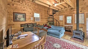L’intérieur d’un chalet accueillant, avec un coin repas, un canapé bleu, un escalier en colimaçon et un poêle à bois.