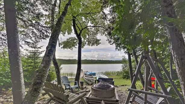 Un terrain de camping équipé d’un foyer, de chaises et offrant une vue sur un lac.