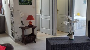 Ett vardagsrum med en mörk soffa, ett litet bord med en lampa och ett stort fönster.