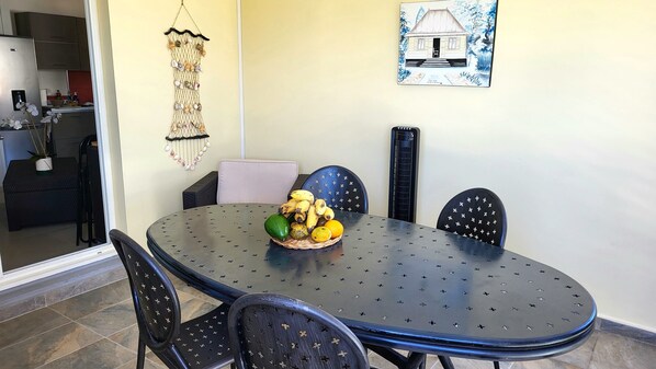 Un coin repas avec une table ronde, quatre chaises et un panier de fruits posé sur la table.