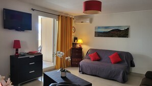 Ett hotellrum med en säng, en tv, ett skrivbord med en lampa, en byrå, ett fönster med gardiner, en klocka och en tavla på väggen.