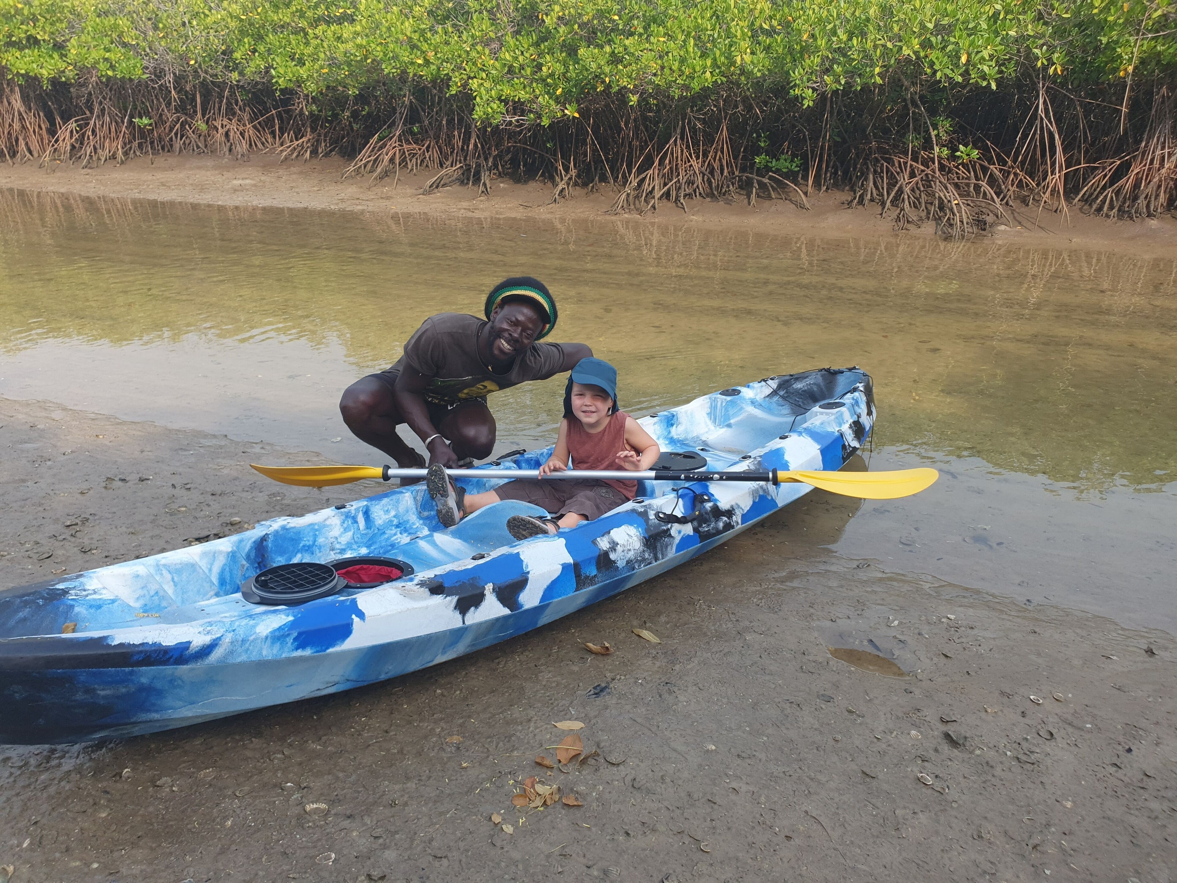 A blue kayak with a child and an adult on a sandy shore.