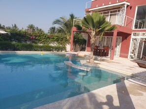 A swimming pool with clear blue water, surrounded by a red building with white windows and balconies.