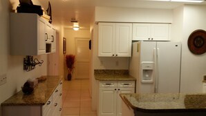 Una cocina con armarios blancos, encimeras de granito, un refrigerador y un dispensador de agua.