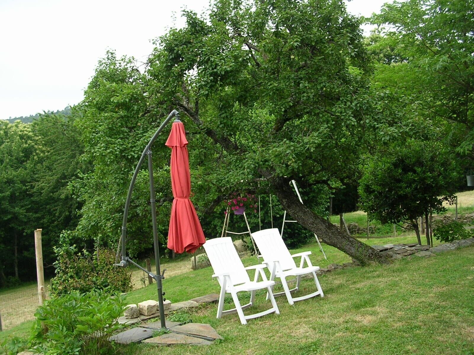 A garden with two white chairs and a red umbrella.