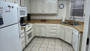 Cucina con mobili bianchi, un forno a microonde, un fornello e un lavello.