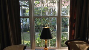 A room with two armchairs, a small table with a lamp, and a large window with curtains.
