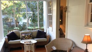 A cozy room with a ceiling fan, wicker furniture, a small table, and a view of greenery outside.