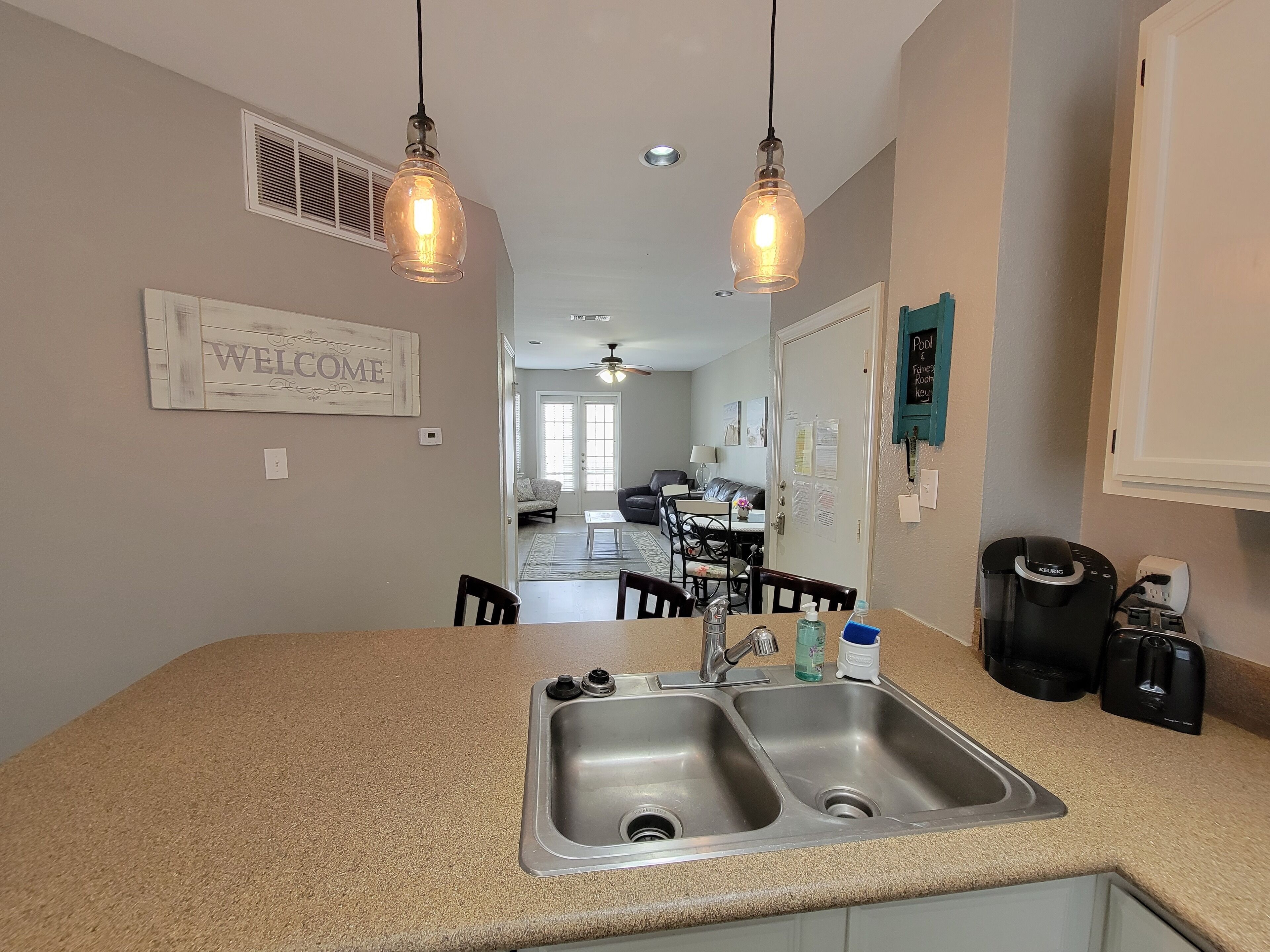 A kitchen with a double sink, a coffee machine, and a refrigerator.