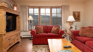 A living room with a red sofa, a wooden cabinet with a television, and a large window with curtains. - Enjoy each season's weather in historic Manchester.   Plenty to do year round!! (Manchester)