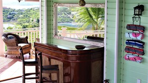 A wooden bar area with wicker furniture, a view of a lush landscape, and a wall-mounted lantern. - 4 bedroom, 4 bathroom. Private Pool, Ocean views. Chocolate Hole, Cruz Bay. (St. John, VI)