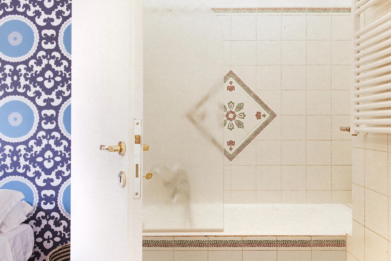A bathroom with a white bathtub, a patterned wall, and a tiled shower area.