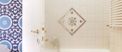 A bathroom with a white bathtub, a patterned wall, and a tiled shower area.