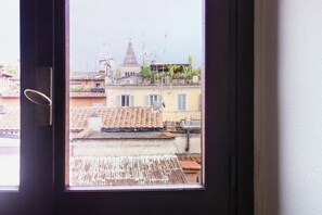 A window view of a building with a tiled roof, a bell tower, and some greenery on the roof.