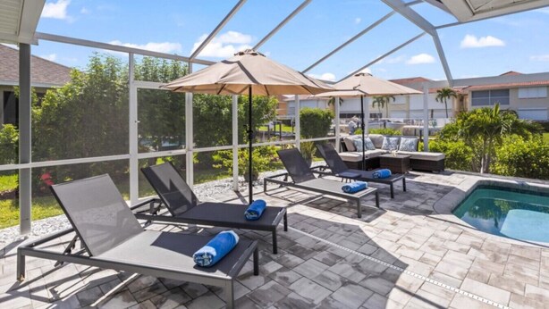 Un espacio exterior techado con sillones de descanso y sombrillas, piscina y vistas de edificios circundantes.