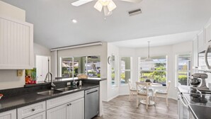 Una cocina moderna con armarios blancos, encimera negra y una zona de comedor con mesa y sillas.