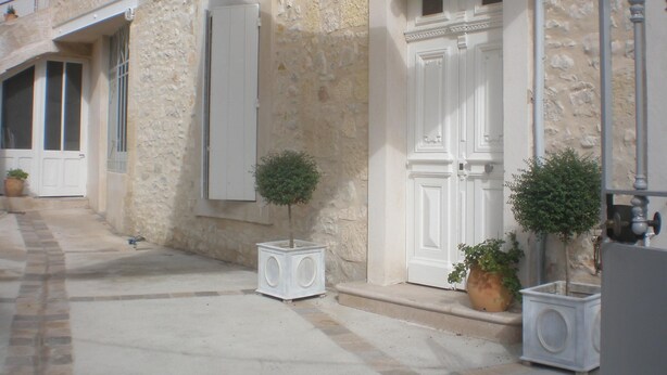 A stone building with a white door, two potted plants, and a white speaker on the ground.