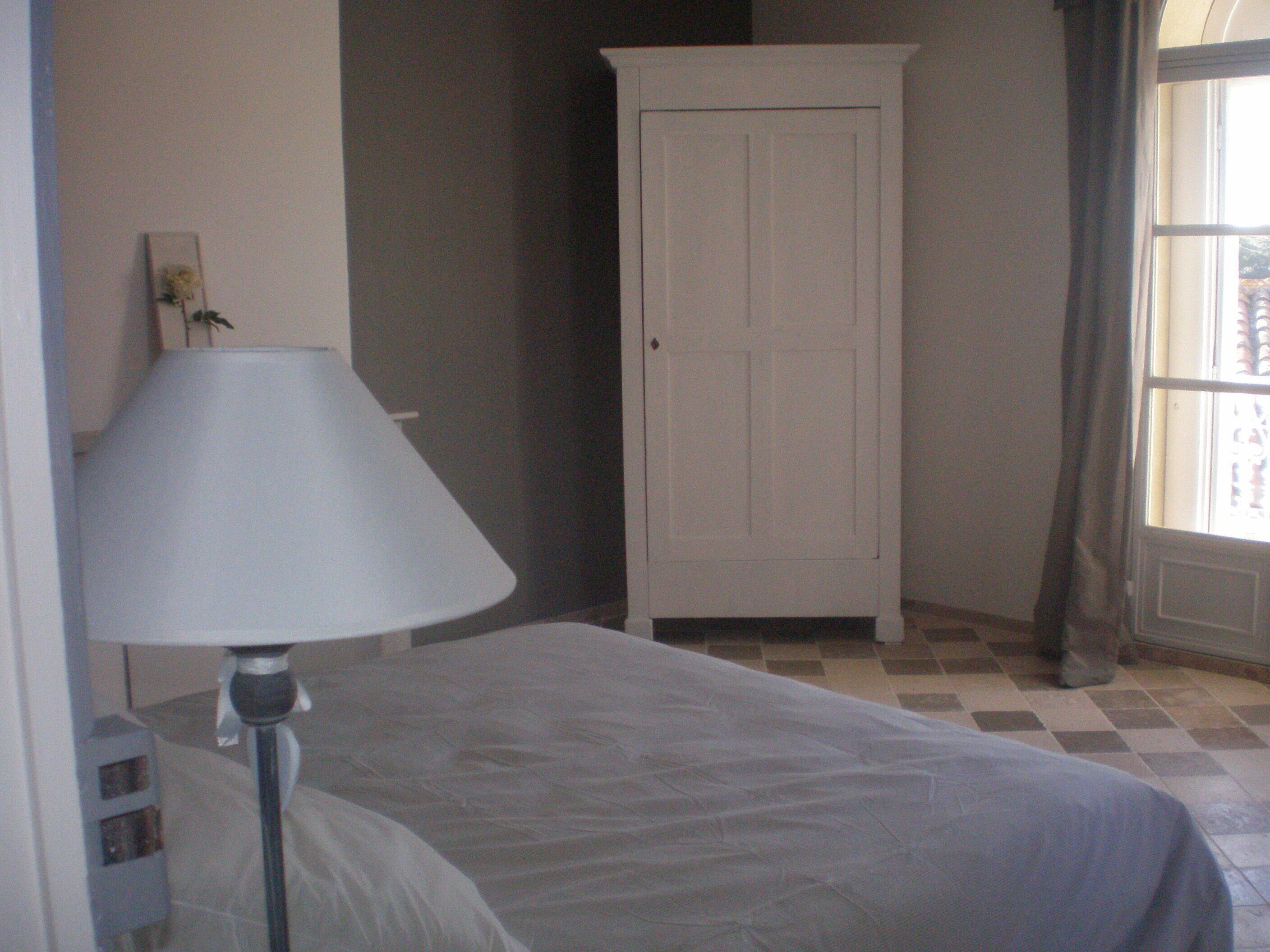 A bedroom with a bed, a bedside lamp, a wardrobe, and a window.