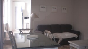A dining area with a glass table, chairs, a sofa, and a lamp.