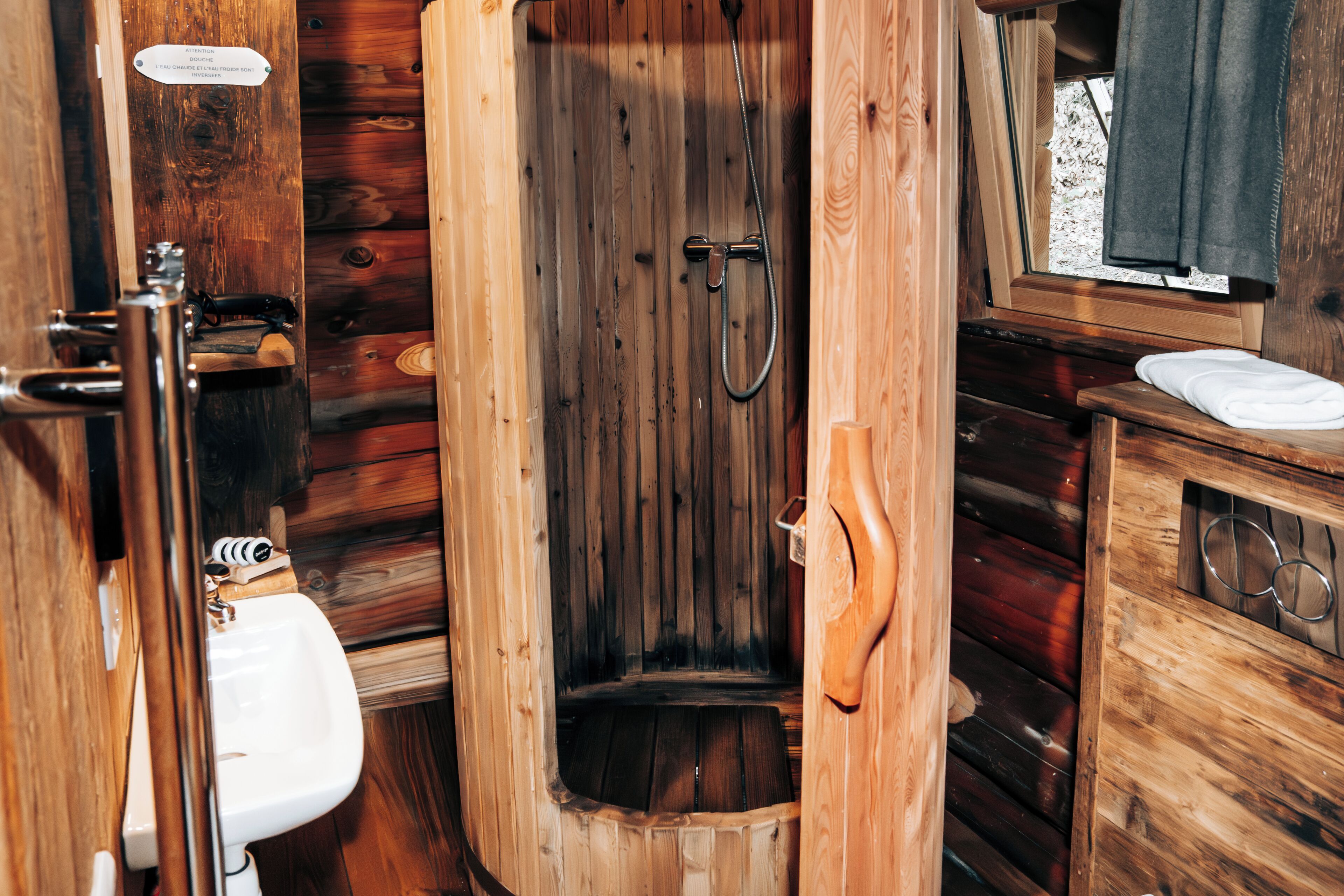 Une salle de bain rustique, avec des murs en bois, une cabine de douche en bois, un lavabo et un porte-serviettes.