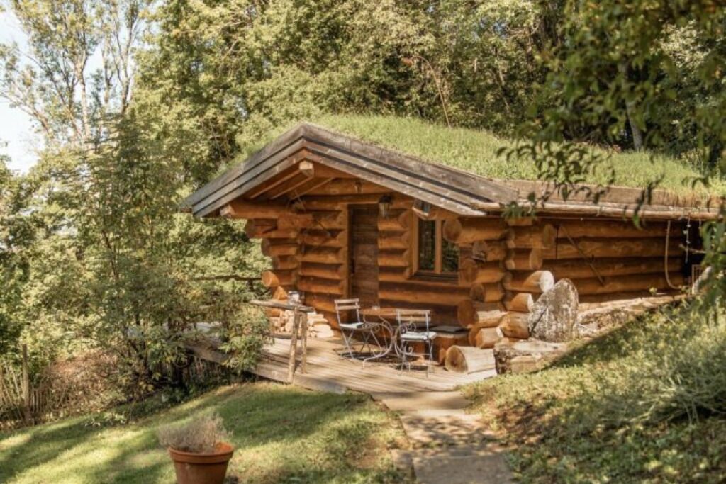 Une cabane rustique en rondins de bois, dotée d’une véranda, d’une petite table et de deux chaises.