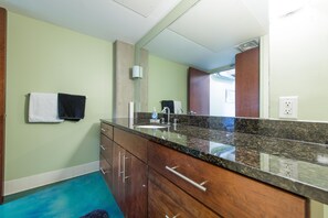 A bathroom with a granite countertop, wooden cabinets, a white sink, and a mirror.